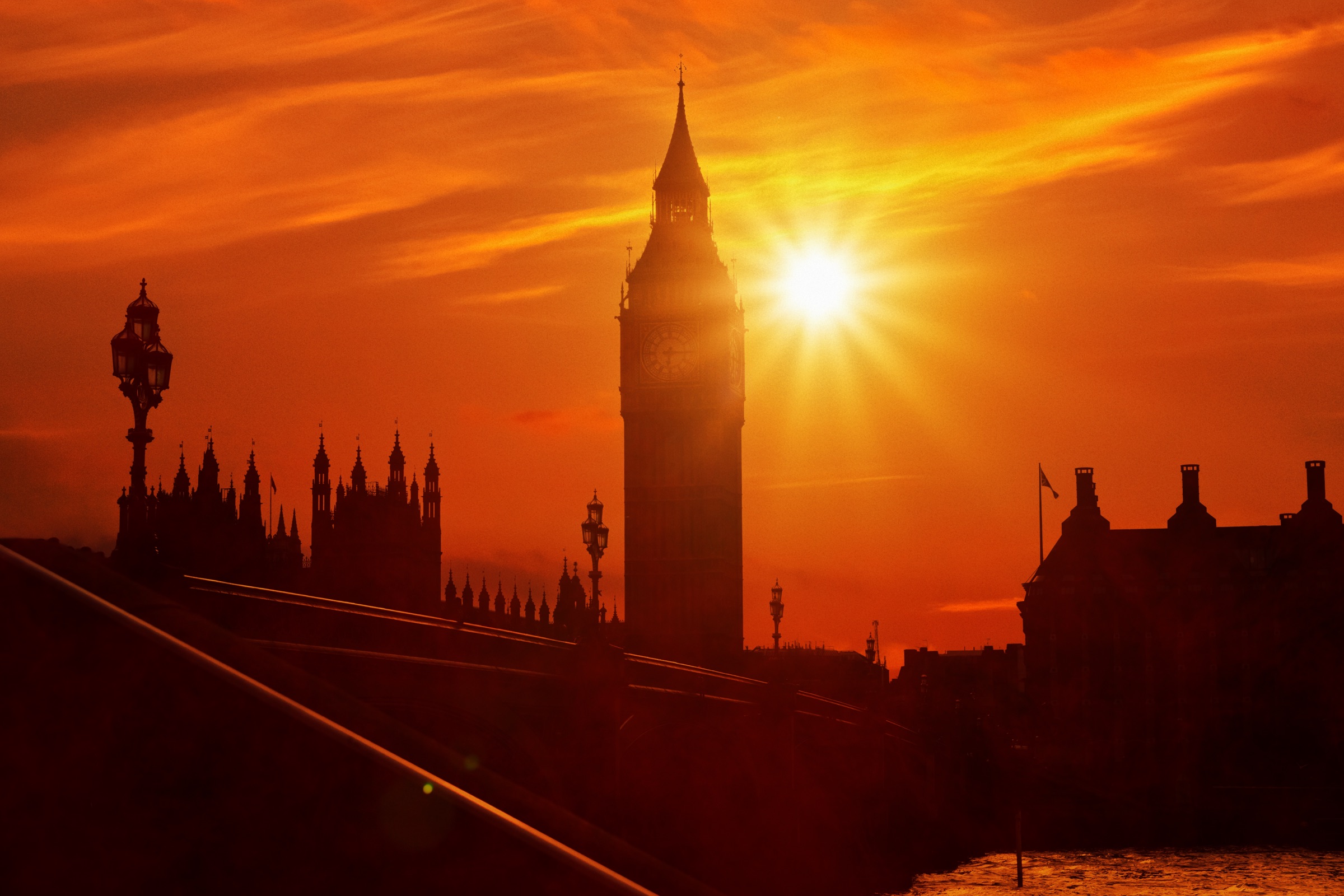 Westminster and Big Ben in silhouette under a blazing orange sky, the sun burning through the haze over London.