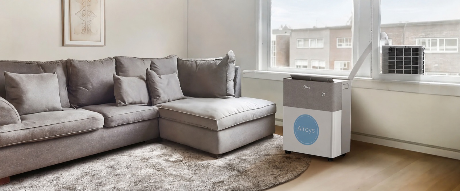 An Aireys-branded portable split air conditioner standing beside the window of a bright living room, its hose running to a compact outdoor unit on the sill — nothing drilled, nothing fixed to the building.