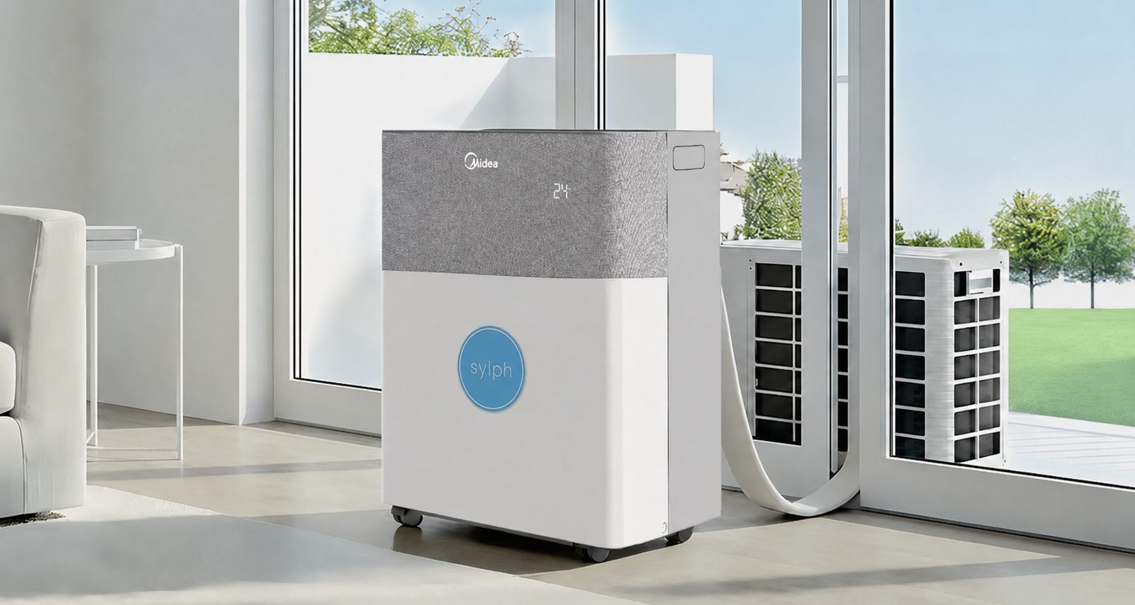 A Midea PortaSplit air conditioner wearing our roundel, standing on its castors in a bright living room beside patio doors. Its hose runs out through the open door to a compact outdoor unit sitting on the terrace — no bracket, nothing fixed to the building.